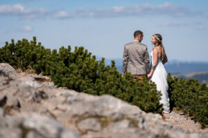 Hochzeit Bergshooting Christina und Michael - Brautpaar steht auf einem Berg in der Natur - Bräutigam und Braut schauen in die Ferne mit dem Rücken zur Kamera