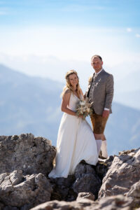 Hochzeit Bergshooting Christina und Michael - Brautpaar steht auf einem Berg in der Natur - Bräutigam und Braut schauen gerade aus in die Kamera