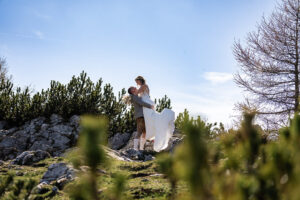 Hochzeit Bergshooting Christina und Michael - Brautpaar steht auf einem Berg in der Natur - Bräutigam hebt Braut nach oben