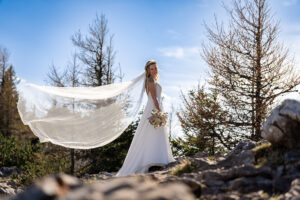 Hochzeit Bergshooting Christina und Michael - Braut steht auf einem Berg, der Wind bläst durch ihren Schleier